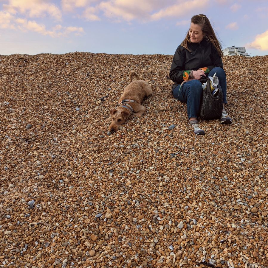 woman sitting on shingle beach with a dog.