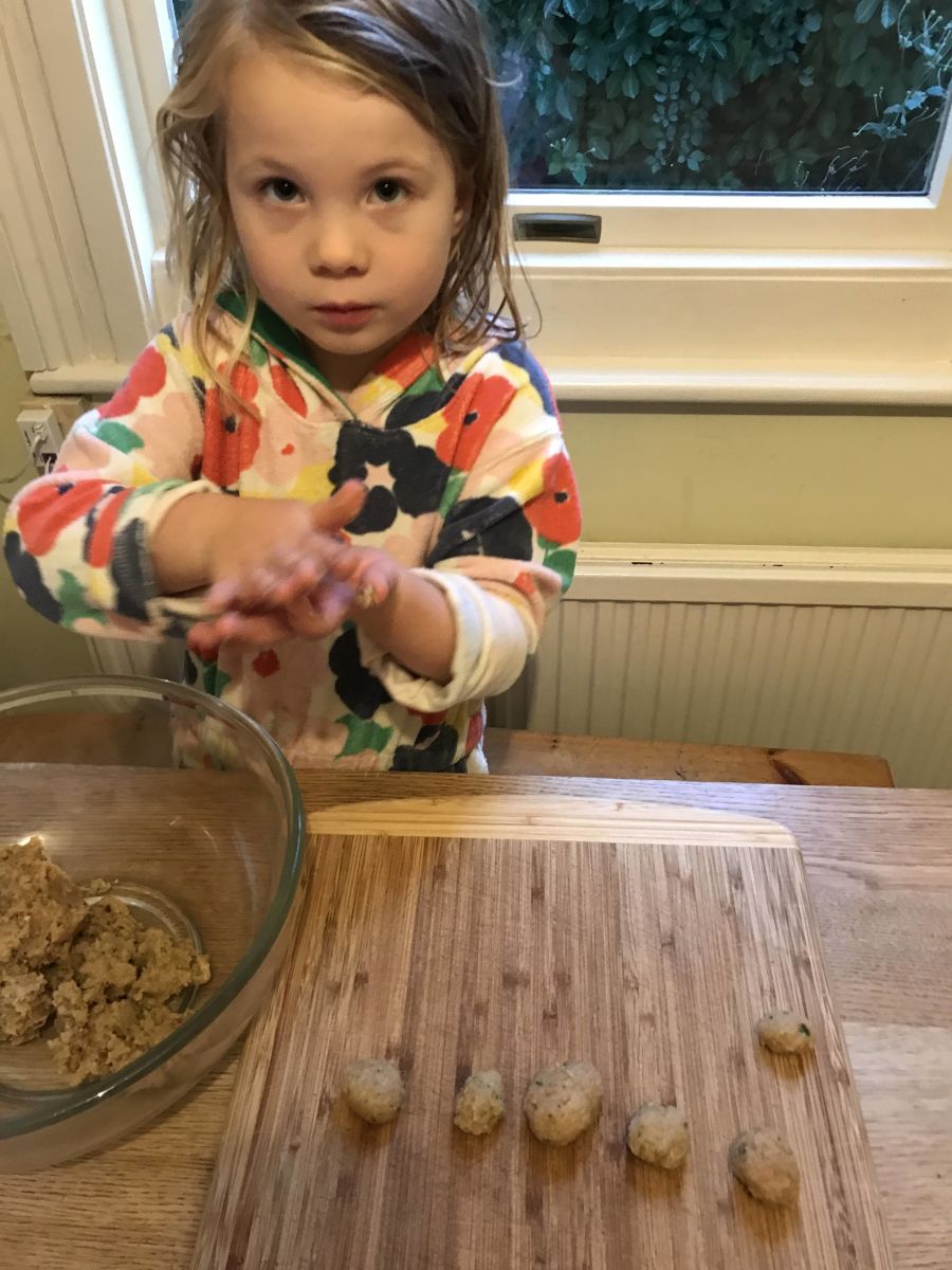young child rolling meatballs with their hands.