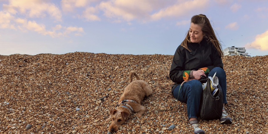 woman sitting on shingle beach with a dog.